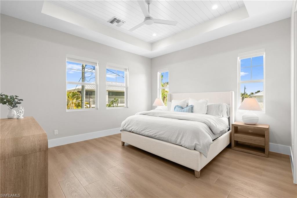 Bedroom with visible vents, baseboards, light wood-style floors, and a raised ceiling. virtually edited photo