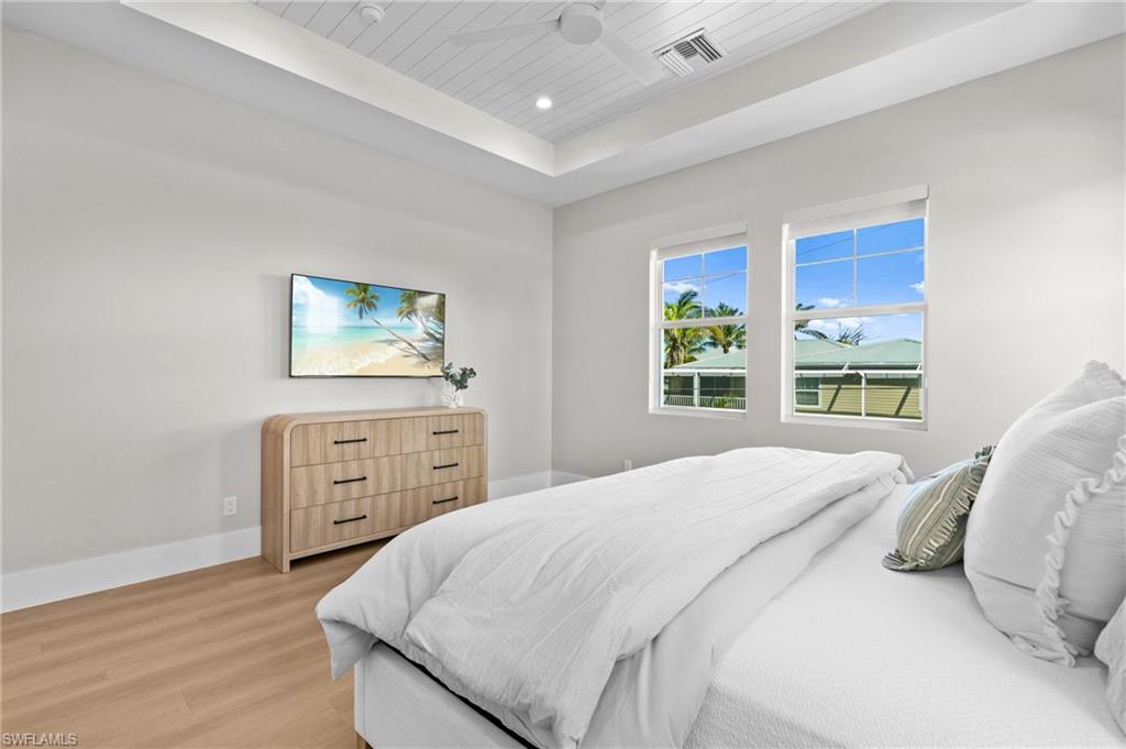 Bedroom featuring light wood finished floors, a raised ceiling, visible vents, baseboards, and wood ceiling. virtually edited photo