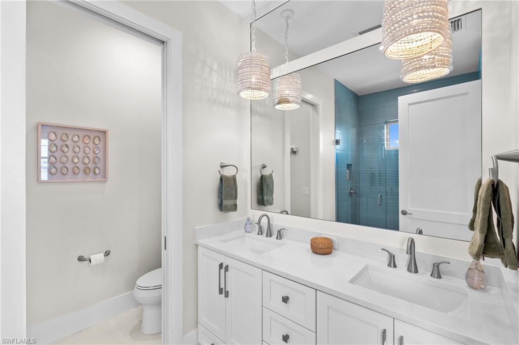 Bathroom with toilet, double sinks, tile patterned floors, and a stall shower. virtually edited photo