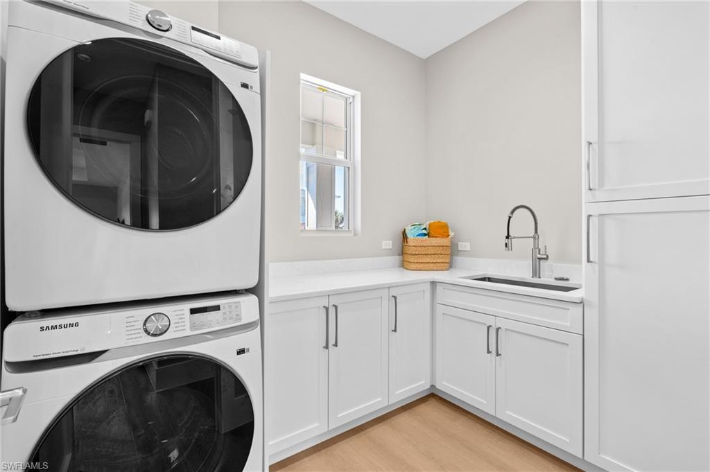 Laundry room, washer/dryer, a sink, light wood-style floors, and cabinet space. virtually edited photo