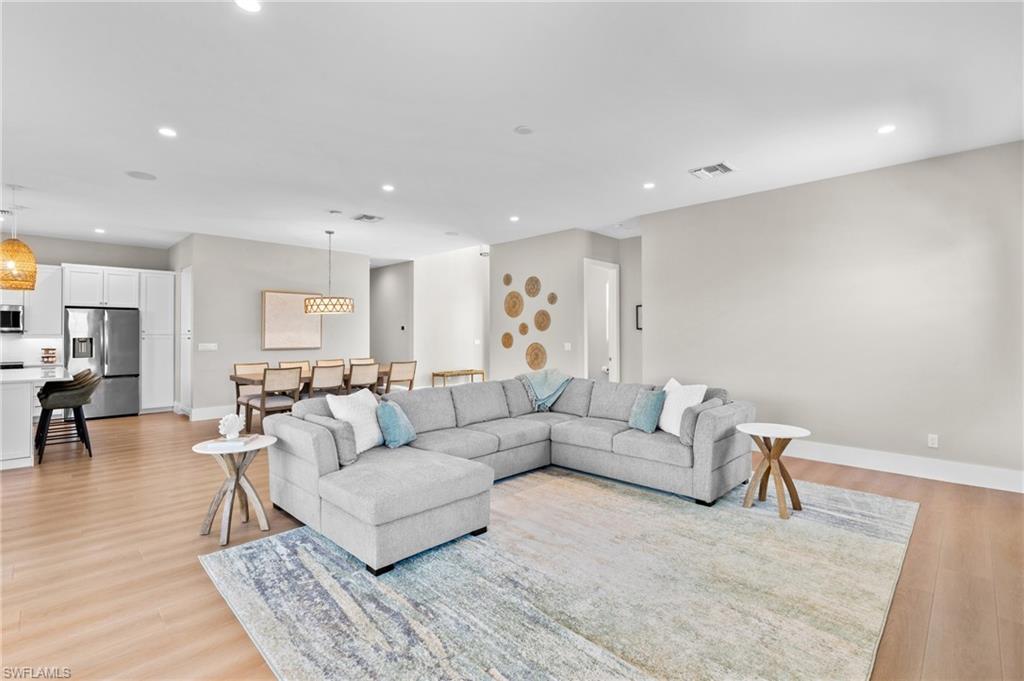 Living area with baseboards, light wood finished floors, visible vents, and recessed lighting. virtually edited photo