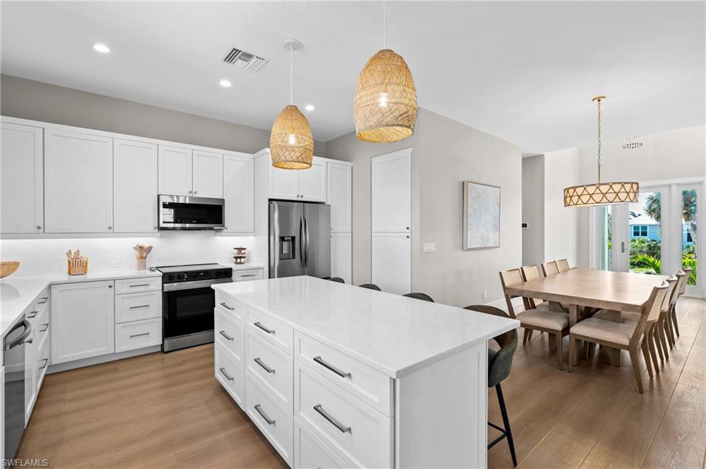 Kitchen featuring stainless steel appliances, a breakfast bar, visible vents, a center island, and light wood-style flooring - virtually edited photo