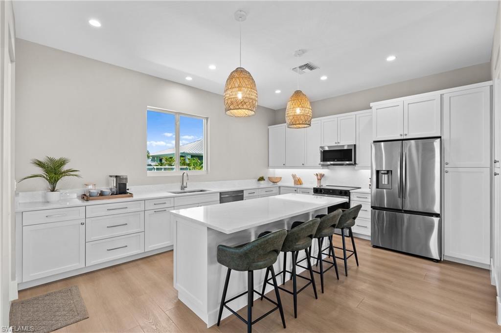Kitchen with stainless steel appliances, light wood-style flooring, a sink, visible vents, and a breakfast bar - virtually edited photo