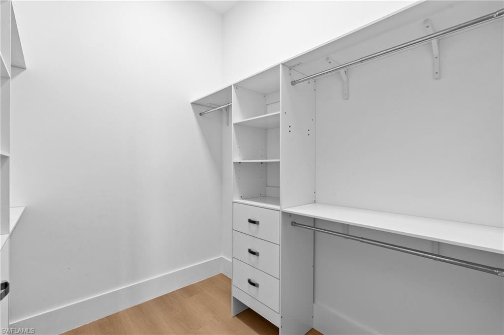 Spacious walk-in closet featuring light wood-type flooring. virtually edited photo