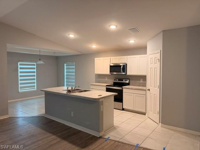 Kitchen featuring an island with an integrated sink, white shaker cabinetry, stainless steel appliances, and light-toned countertops