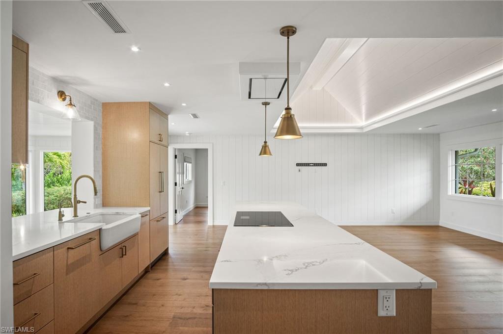 Open chef's kitchen features CUSTOM WHITE OAK STYLE CABINETRY, QUARTZ COUNTERS, and top-of-the-line appliances, including an induction cooktop, WOLF vent hood, wall oven, microwave drawer, and dual refrigerator drawers built into the oversized island.