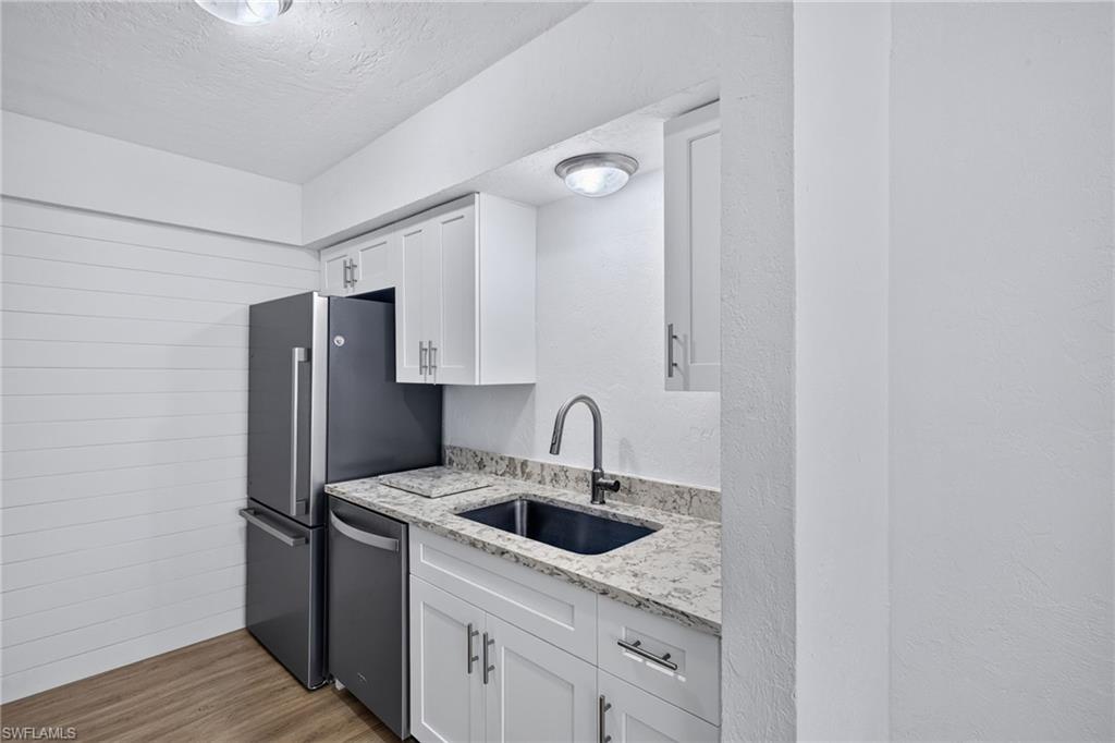Kitchenette featuring white shaker cabinetry, light-toned stone-finish countertops, stainless steel appliances, and wood-finish flooring