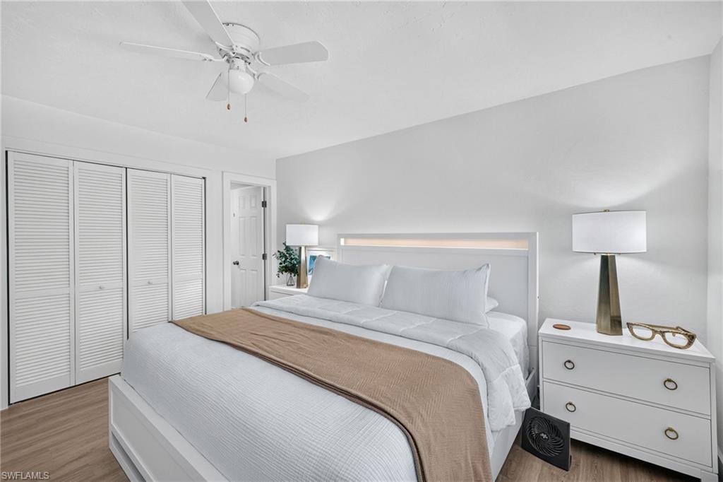 Bedroom featuring wood-finish flooring, louvered bi-fold closet doors, a ceiling fan with integrated lighting, and a white paneled headboard with accent lighting