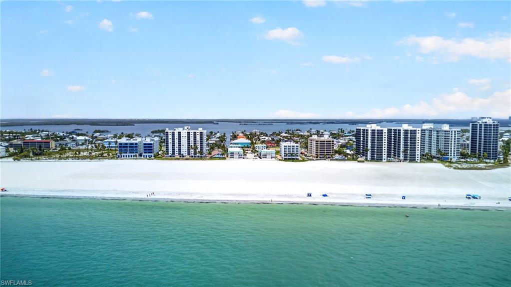 Expansive white sand beach with turquoise waters, featuring multiple beachfront high-rise buildings and distant coastal development