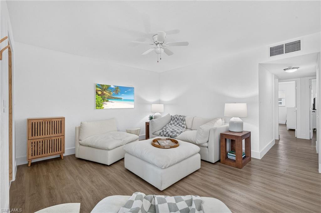 Spacious living area featuring light wood-finish flooring, white walls, and a ceiling fan