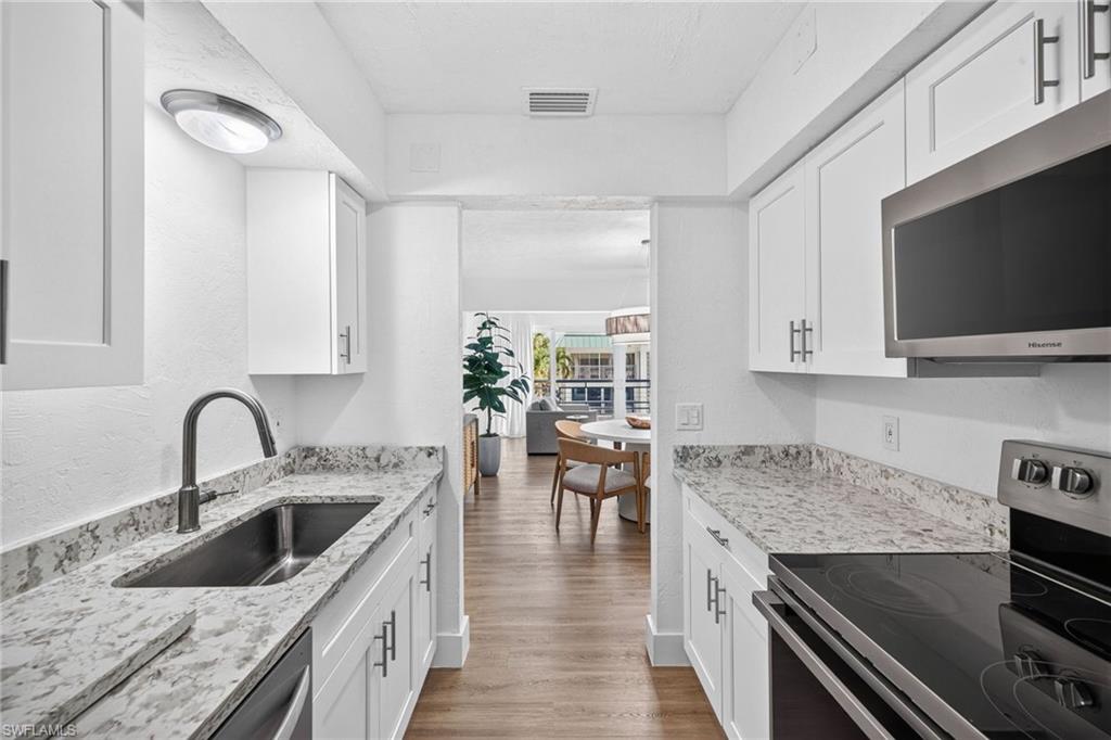 Galley kitchen featuring white cabinetry, light-toned countertops, stainless steel appliances including an over-the-range microwave and electric range, and wood-finish flooring
