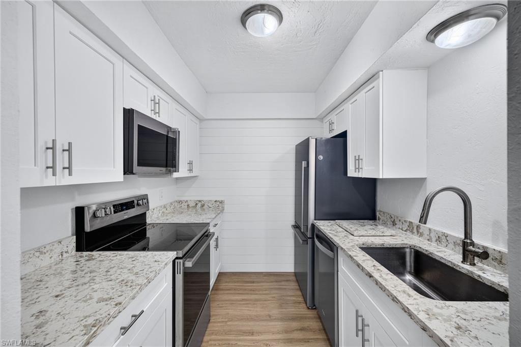 Contemporary kitchen featuring white cabinetry, light-toned countertops, stainless steel appliances, and wood-finish flooring