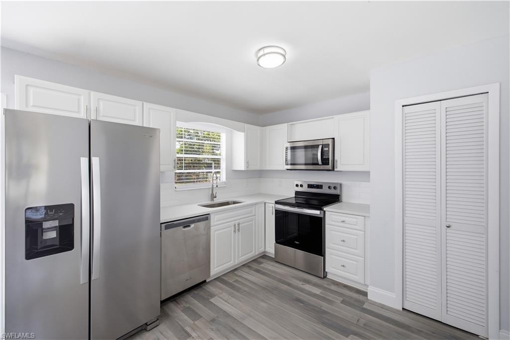 Modern kitchen featuring white cabinetry, stainless steel appliances, light countertops, a white subway tile backsplash, and wood-finish flooring