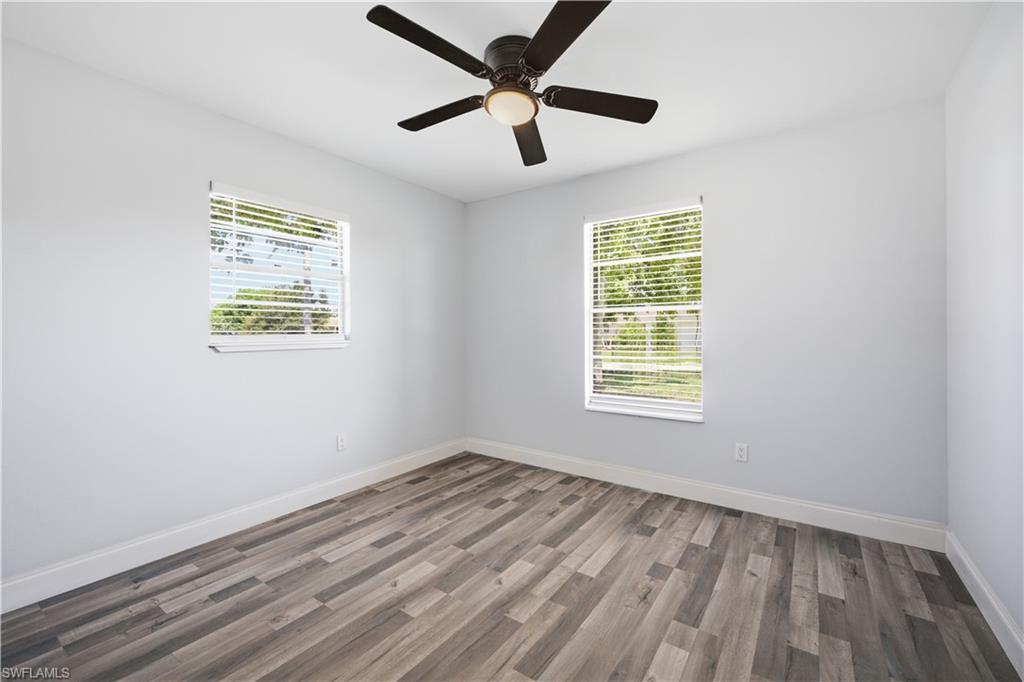 Spacious room featuring wood-finish flooring, two windows with blinds, a ceiling fan with integrated lighting, and light-toned walls