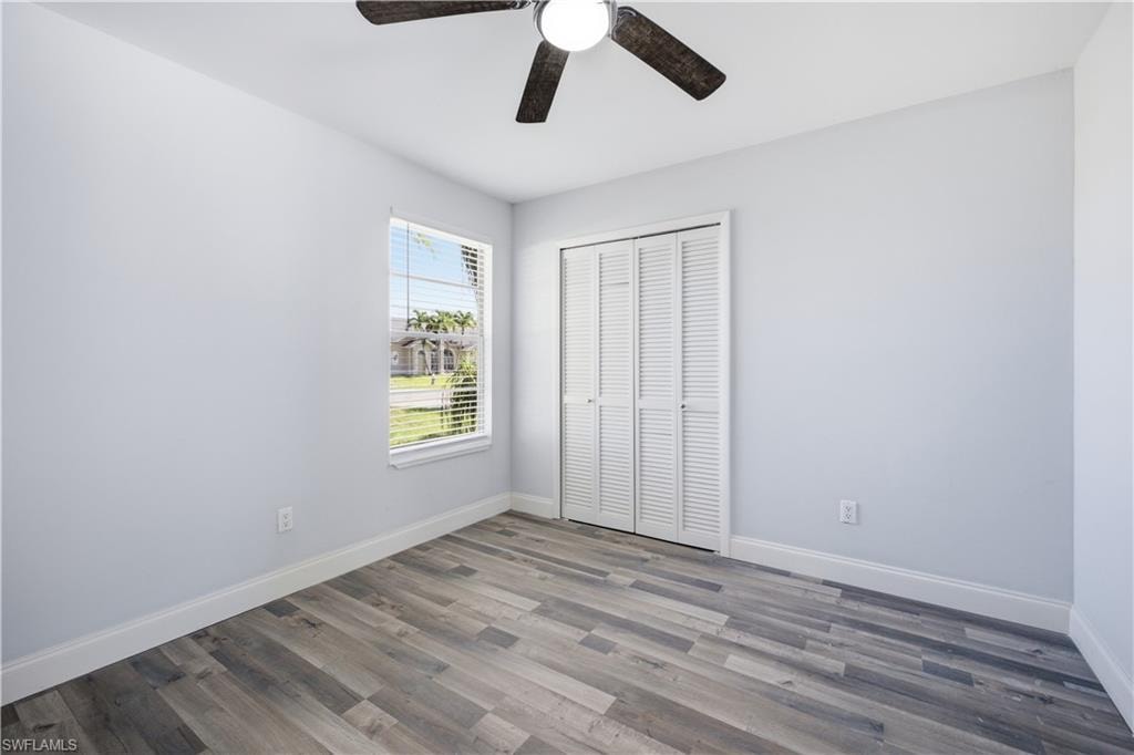 Room featuring wood-finish flooring, a window with blinds, and white louvered bifold closet doors