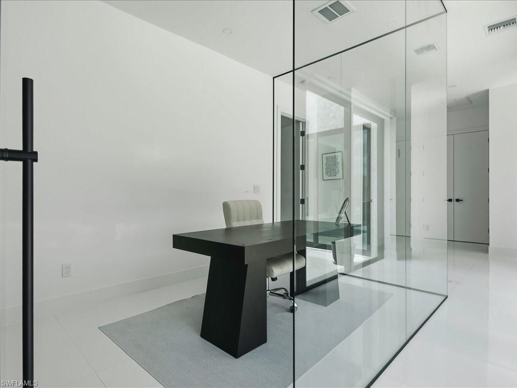 Glass-enclosed office space featuring a minimalist black desk, white walls, and light-toned flooring