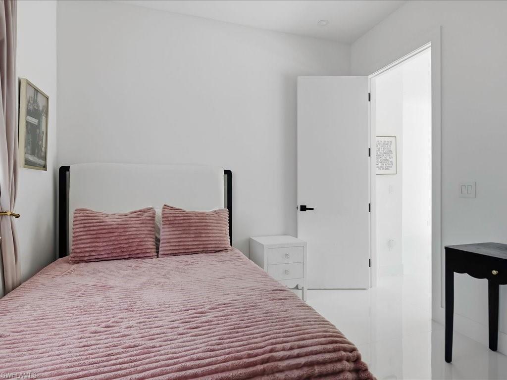 Room featuring bright white walls, white glossy flooring, a white headboard, a white nightstand, and a white interior door with matte black hardware