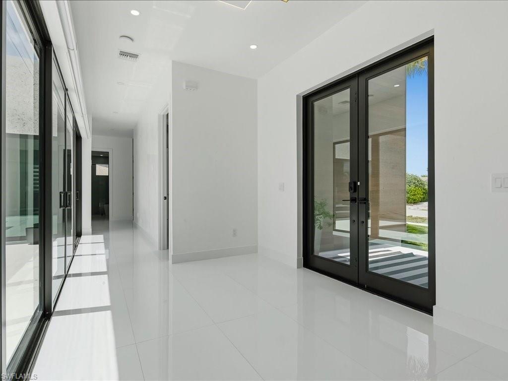 Entryway featuring dual glass panel doors, high-gloss tile flooring, recessed ceiling lighting, and a hallway with sliding glass doors
