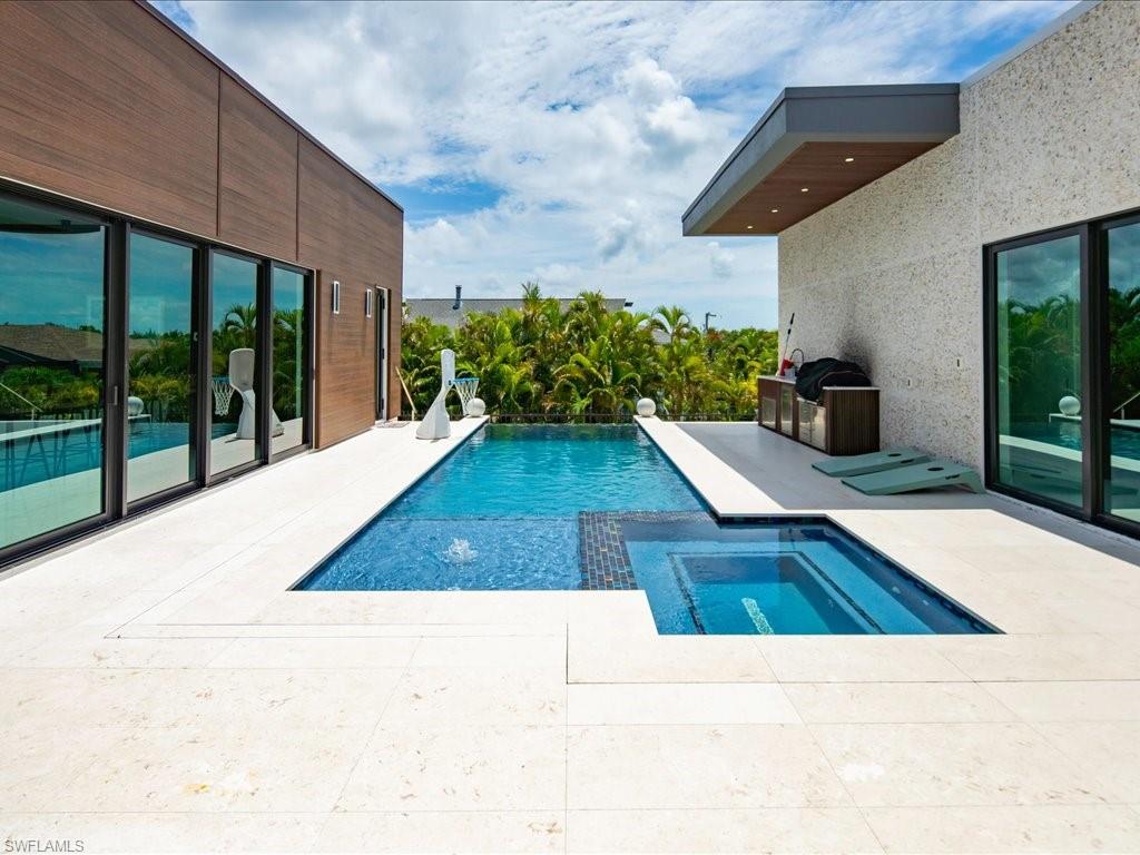Contemporary exterior featuring a rectangular pool with integrated spa, light-toned patio pavers, and expansive glass sliding doors
