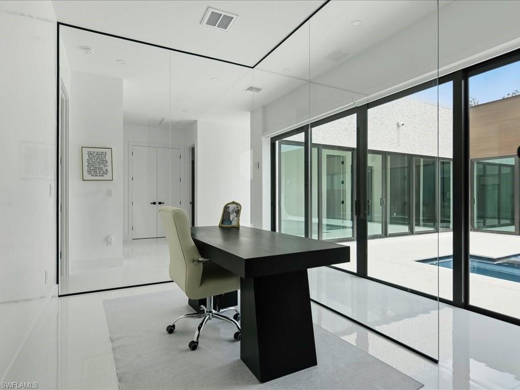 Spacious room featuring glossy white flooring, floor-to-ceiling glass paneling, and an expansive sliding glass door system opening to an exterior courtyard with a pool