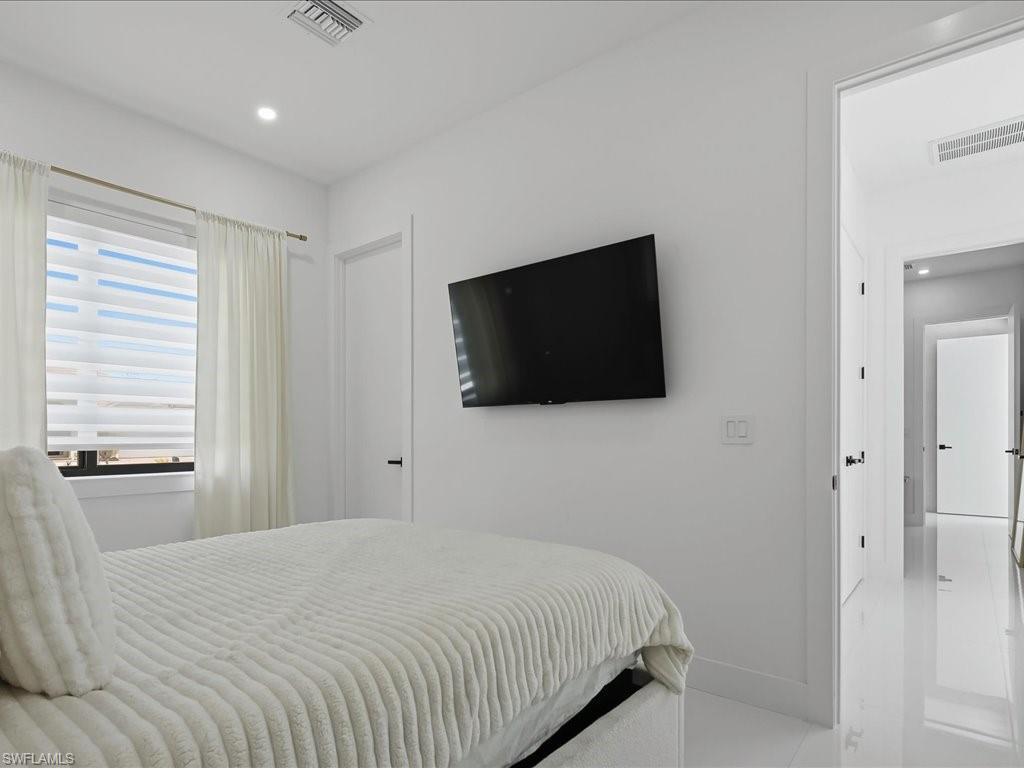 Bright room featuring a window with layered shades and sheer curtains, recessed lighting, and a wall-mounted television
