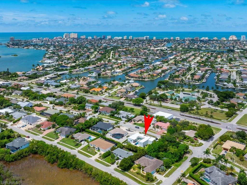 Aerial perspective showcasing a residential area with canal access, mature landscaping, coastal proximity, and a clear blue sky