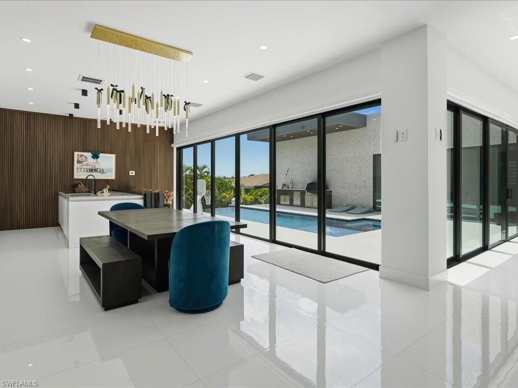 Open-concept interior featuring large format white tile flooring, a contemporary linear chandelier, and a wood-paneled accent wall