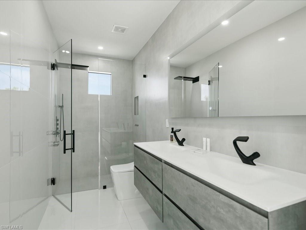 Modern bathroom featuring a double vanity with matte black faucets, a frameless mirror, and recessed lighting