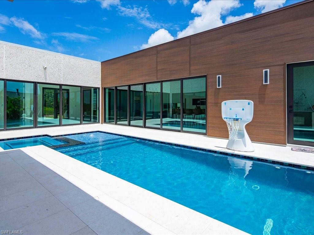 Expansive outdoor living area featuring a rectangular pool with an integrated spa, white tile coping, and a surrounding patio