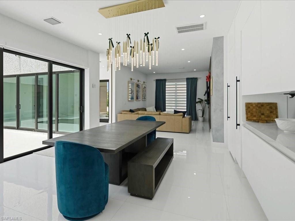 Contemporary dining area with a linear chandelier, large format white tile flooring, and sliding glass doors