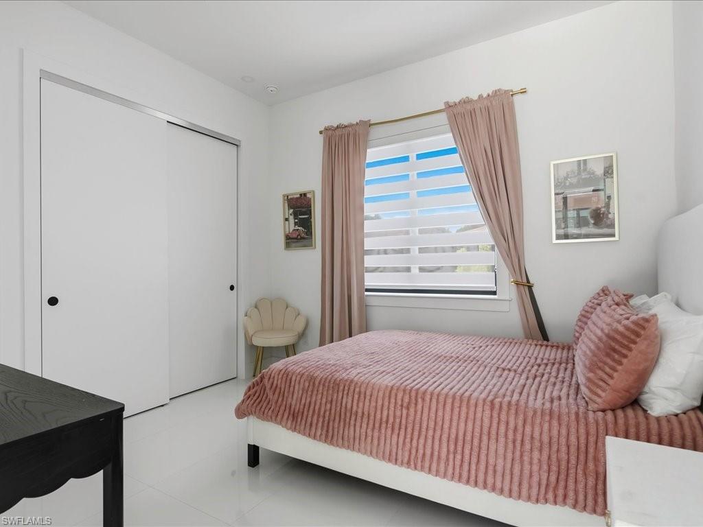 Bright interior space featuring a window with integrated blinds, white tile flooring, and a white sliding door closet