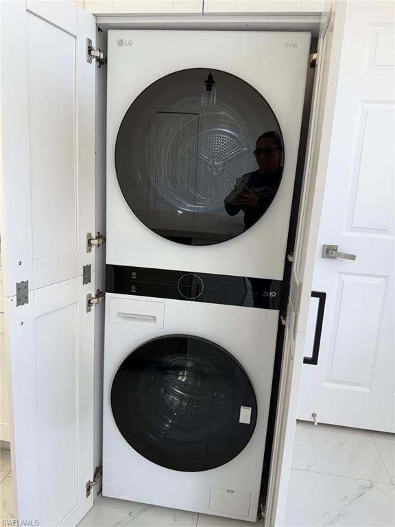 Laundry room featuring stacked washer / drying machine and light marble finish flooring