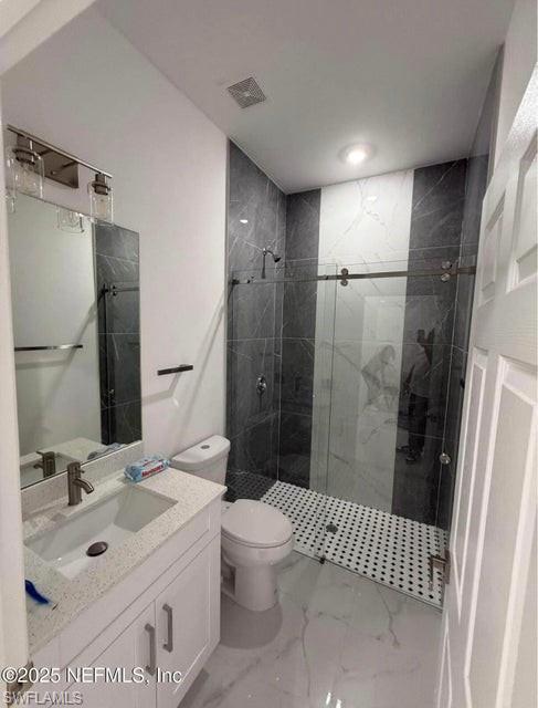 Full bath with vanity, a marble finish shower, and light marble finish floors