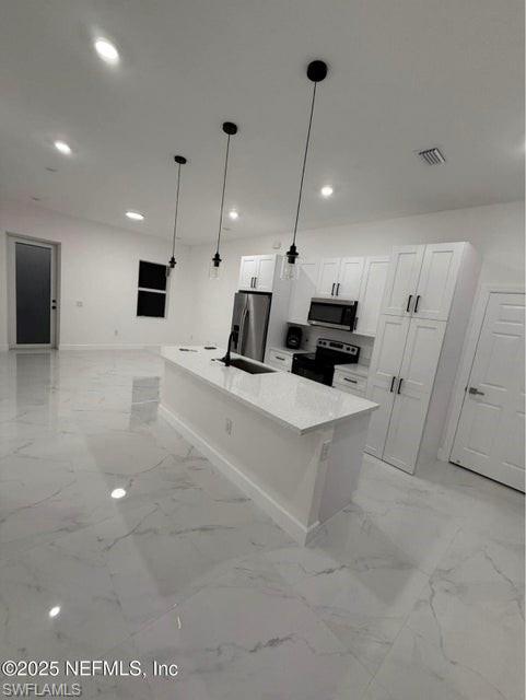 Kitchen with an island with sink, decorative light fixtures, recessed lighting, appliances with stainless steel finishes, and white cabinetry