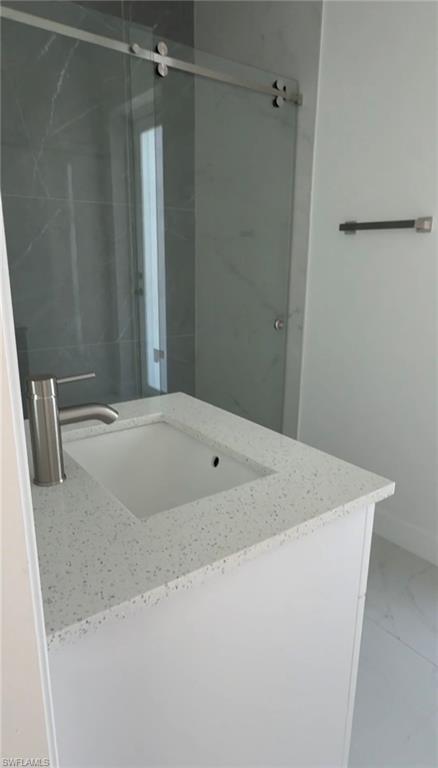 Full bath with vanity, marble look tiles, and a shower stall