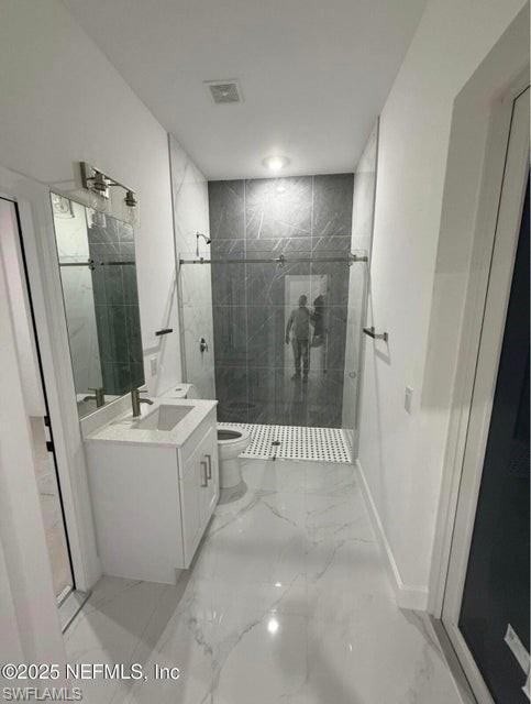 Full bath with a shower stall, vanity, and light marble finish flooring