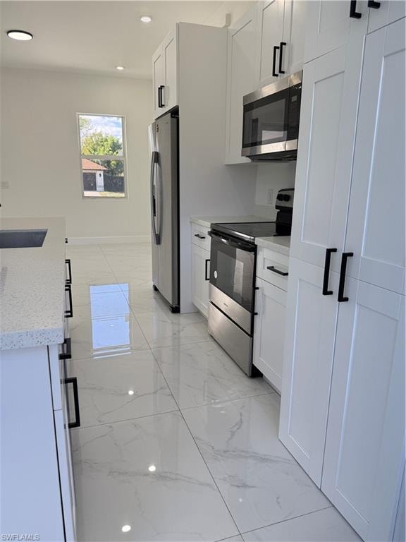 Kitchen featuring light marble finish floors, stove, fridge, light stone counters, and white cabinets