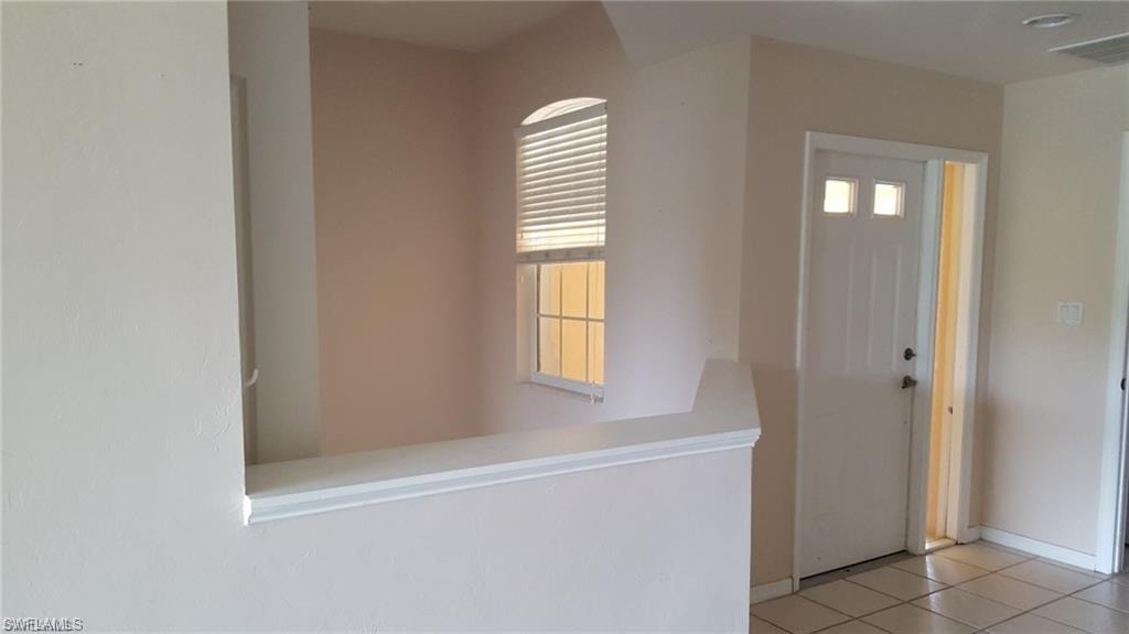 Entryway featuring a white paneled door with glass inserts and a sidelight, neutral wall tones, tile flooring, a half-wall partition, and an arched window with blinds