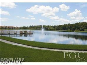 Serene lake with a central fountain, bordered by a wooden dock structure and a paved pathway