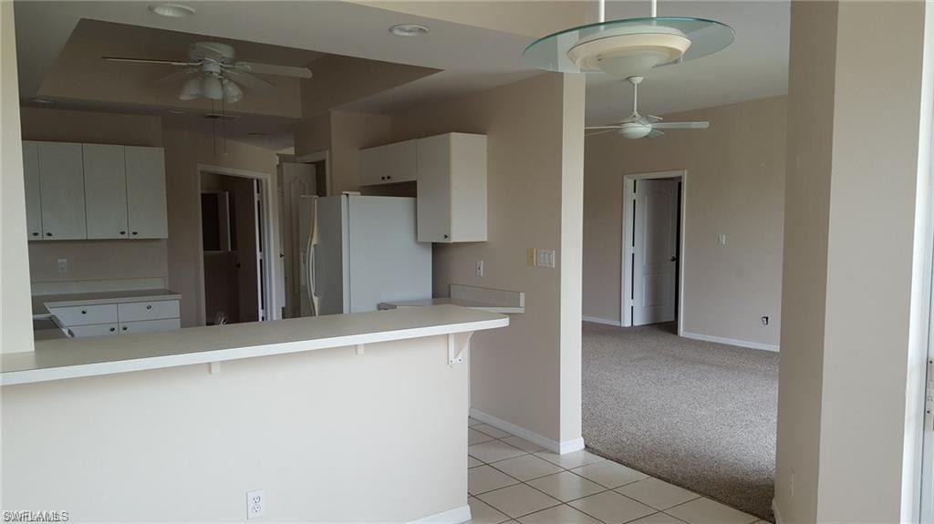 Kitchen featuring white cabinetry and countertops, a peninsula with breakfast bar seating, tile flooring, and a ceiling fan with light fixture