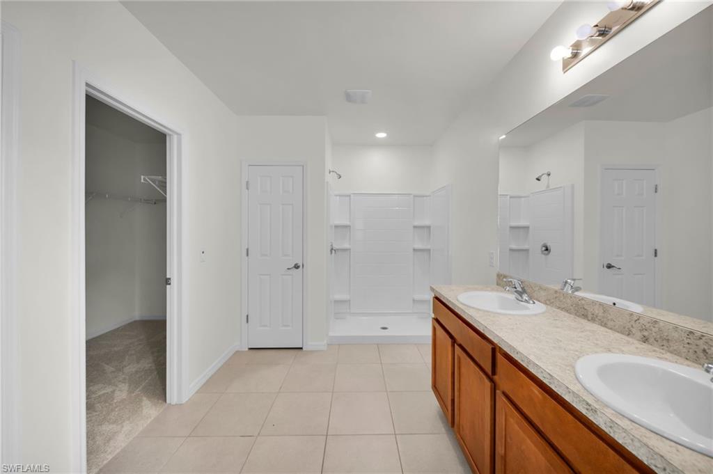 Bathroom featuring a double vanity with wood cabinetry and light-toned countertops, a full-width mirror, and a walk-in shower with white subway tile-style surround