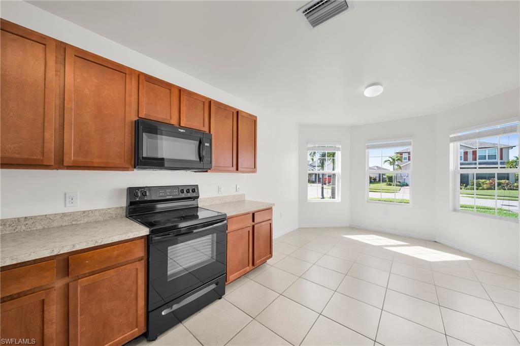 Kitchen and dining area featuring wood-finish cabinetry, black appliances including a range and microwave, light-toned countertops, and tiled flooring