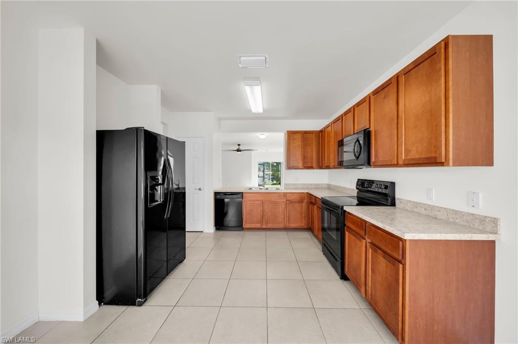 Spacious kitchen featuring extensive wood cabinetry, light-toned countertops, and black appliances