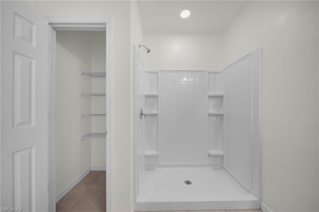 White shower stall with built-in shelving, chrome fixtures, and a recessed ceiling light