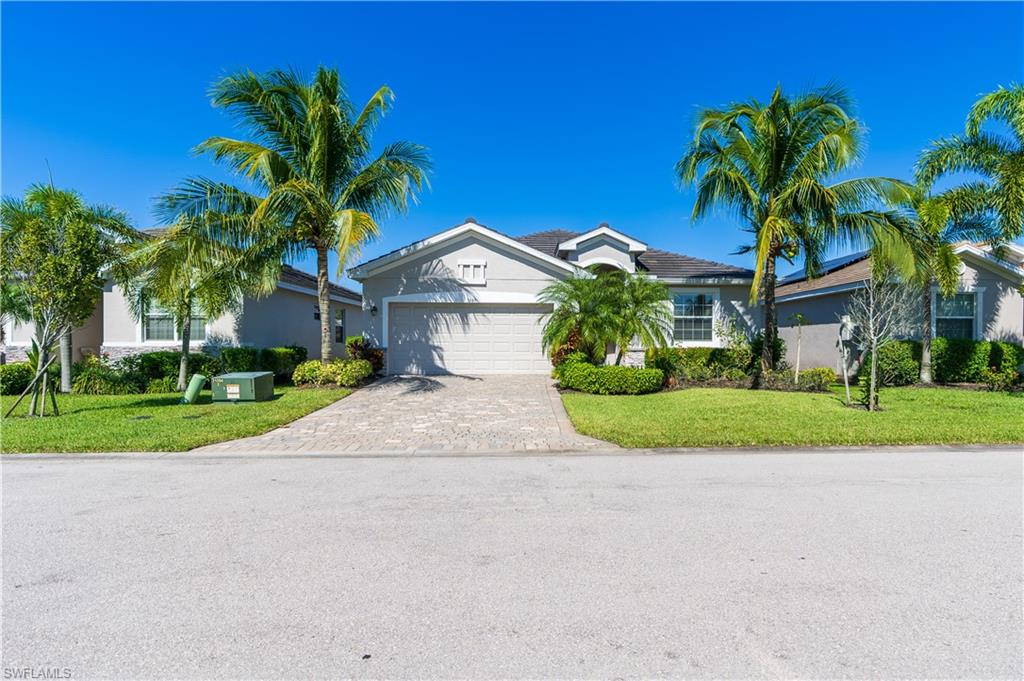 Single-story residence featuring a paver driveway, an attached garage, and mature palm trees