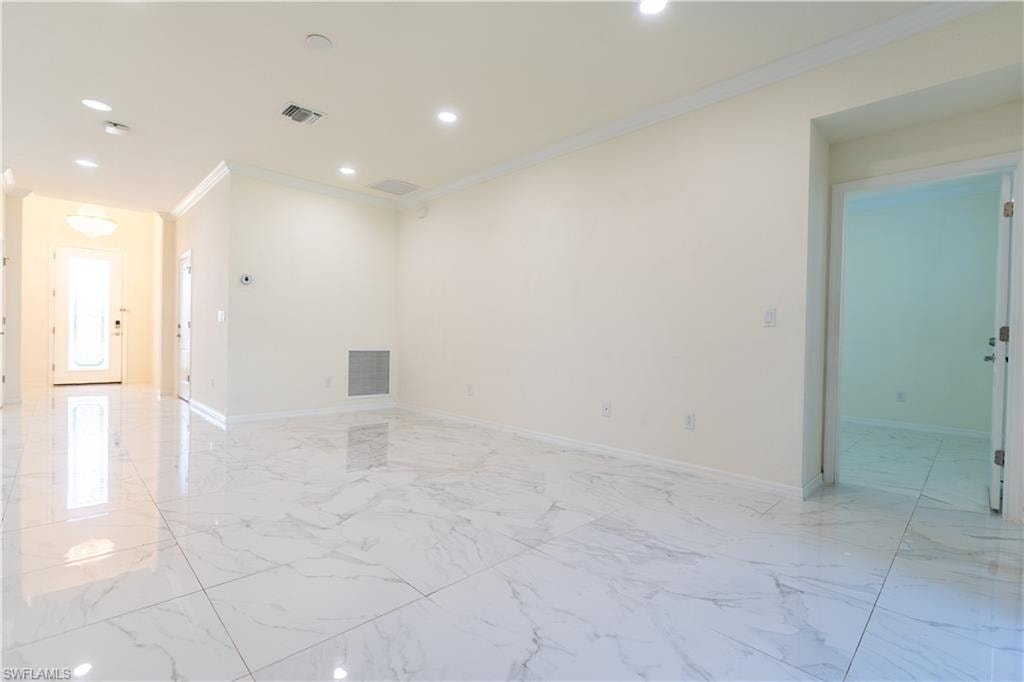Spacious interior featuring large format tile flooring, crown molding, recessed lighting, and a bright entryway with a transom window