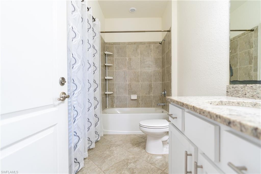 Bathroom featuring a full tub with shower, tiled surround, and a vanity with a light-colored countertop