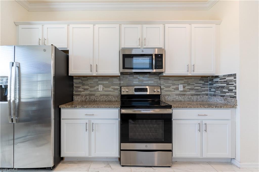 Kitchen featuring white shaker cabinetry, stainless steel appliances, granite countertops, and a mosaic tile backsplash