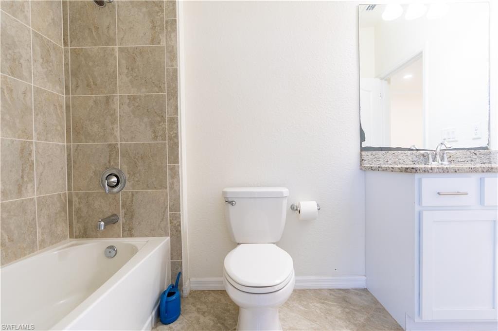 Bathroom featuring a shower-tub combination with tile surround, a toilet, and a vanity with a stone-finish countertop and undermount sink