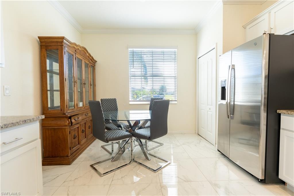 Dining area featuring a window with blinds, white wall paint, crown molding, and large format tile flooring